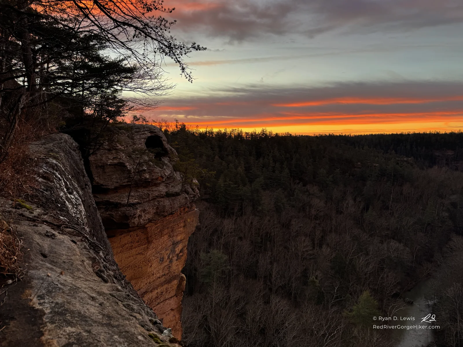 Vivid orange sunrise beside the sandstone at Eagle’s Nest, overlooking forested ridges and a river in the Red River Gorge.